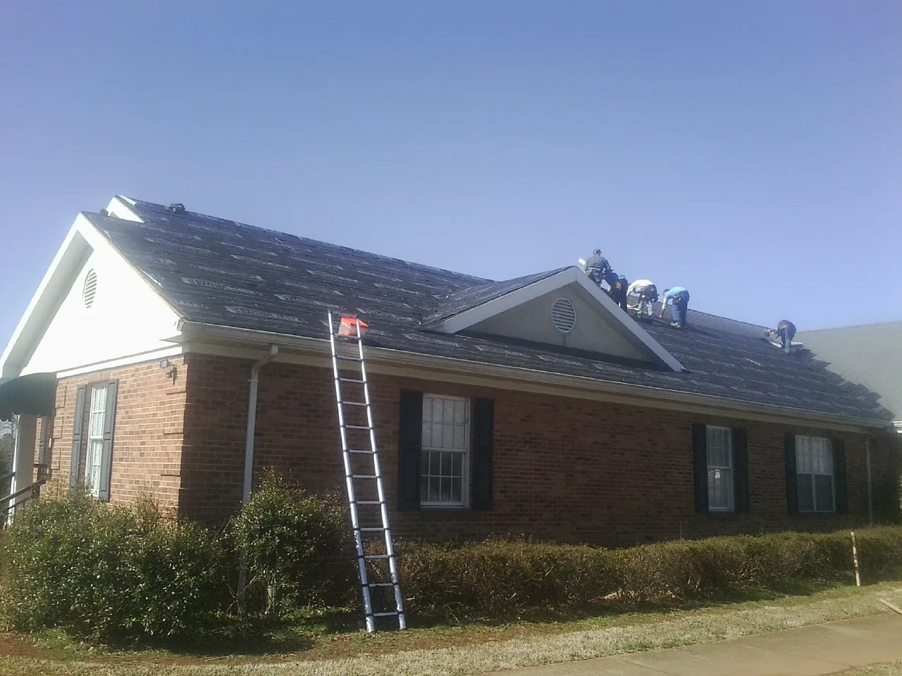 Crew tearing shingles off a brick ranch roof with a ladder set — Emergency Roof Repair work by our crew in Horse Cave