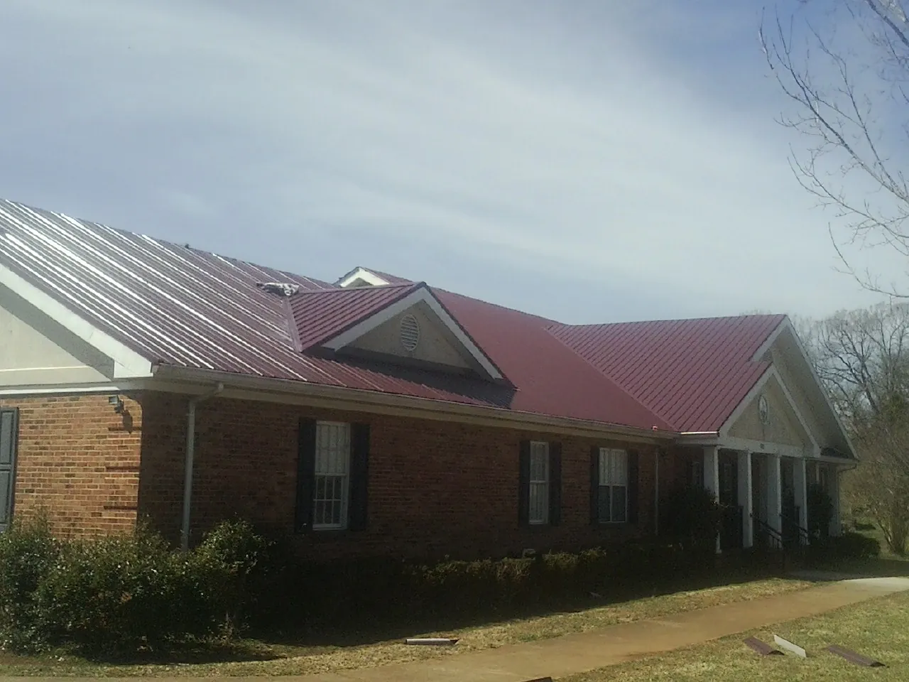 Red metal roof with gabled entries on a long brick building, from a Hail Damage Roof Repair job in Horse Cave