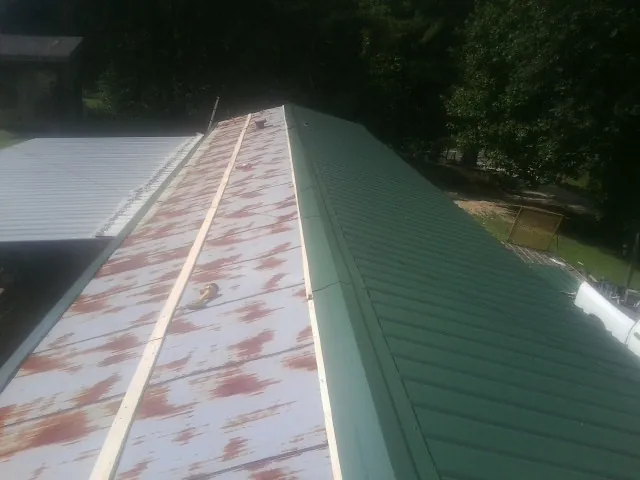 Old rusted panels beside newly installed green metal roofing — Wind Damage Roof Repair by Roofing Brothers in Horse Cave