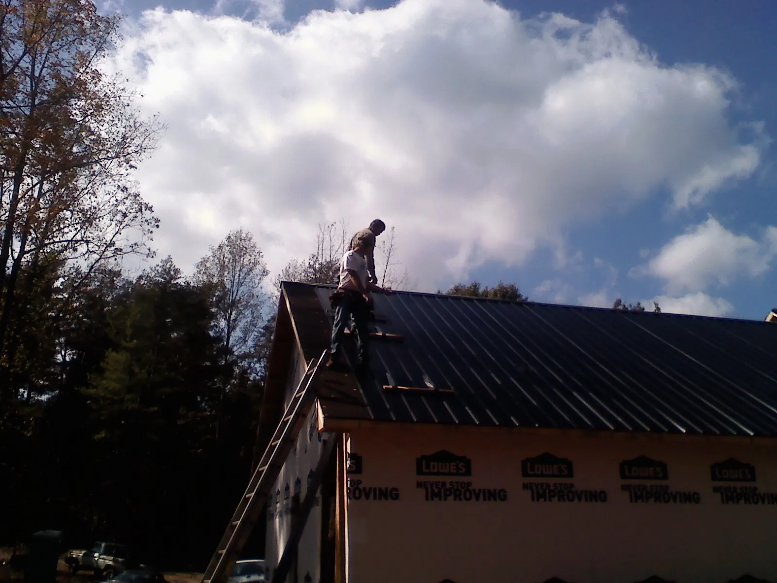 Roofer fastening dark metal panels high against a cloudy sky, from a Roof Inspection job in Horse Cave