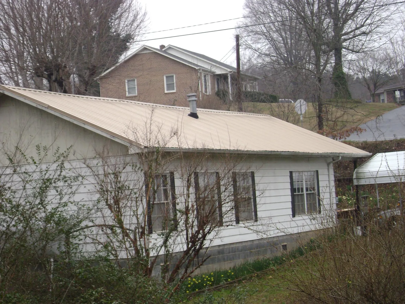 Tan metal roof on a white sided house set into a hillside — Commercial Roofing by Roofing Brothers in Horse Cave
